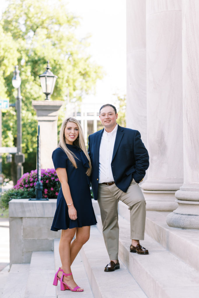 A couple poses for engagement photos on the step of a columned building with formal attire