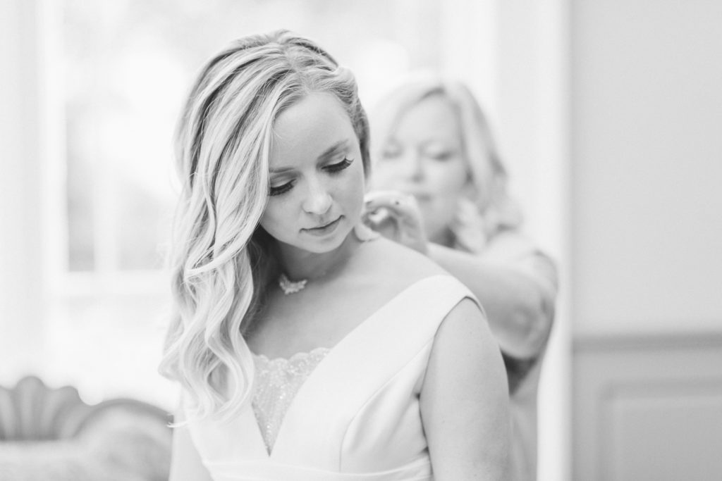 Mother of the bride putting on bride's necklace on a wedding day in black and white film
